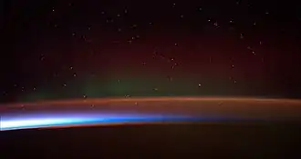 Image 17Earth's atmosphere as it appears from space, as bands of different colours at the horizon. From the bottom, afterglow illuminates the troposphere in orange with silhouettes of clouds, and the stratosphere in white and blue. Next the mesosphere (pink area) extends to just below the edge of space at one hundred kilometers and the pink line of airglow of the lower thermosphere (invisible), which hosts green and red aurorae over several hundred kilometers. (from Earth)