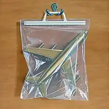 A bag with a gold plane inside hanging from a hook on a wooden background