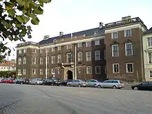 Three story palace with two large wings. Many decorative elements such as cornices, window pediments, and a stone balcony over the entrance.