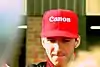 Damon Hill wearing a red baseball cap with sponsors logos signing autographs for fans