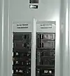Illustration of breaker numbering in a North American type panelboard. Some labels are missing, and some are additional. The numbers on the toggles indicate the rated ampereage before tripping. The top right breaker (Rated at 100&nbsp;A) feeds a sub panel.