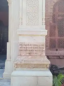 This is a rectangular stone plaque with inscription about laying the cornerstone for Museum - as Jubilee Museum and Technical Institue - by Prince Albert Victor February 3rd 1890. The stone is light in colour, the inscription is in English, in four rows, with black letters. This plaque is built in the decorative pillar at the right side of the Museum entrance.