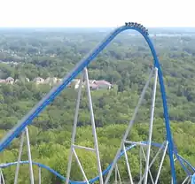 A blue roller coaster's first drop, with a 8 car train about to go down it.
