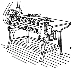 Line drawing of a table-like machine, with many wheels along the near edge, connected to a a larger, belt-powered wheel.